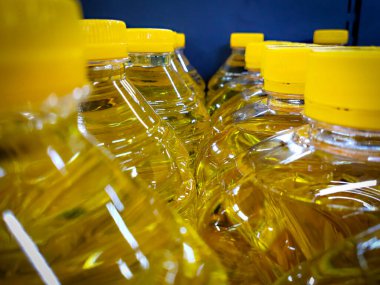 Seçici odaklı yakın çekim, parlak altın sarısı pişirme yağıyla dolu bir sıra berrak plastik şişeyi yakalar, parlak yansıyan ışık ve bulanık bir ön plan ile arkadan aydınlatır..