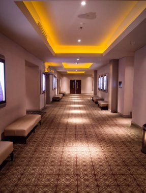 Jakarta, Endonezya - 30 Aralık 2024: Boş bir sinema koridoru desenli halı, oturma düzeni ve neon film tabelasıyla döşenmiştir. Arka planlar ya da eğlence mekanı için mükemmel..
