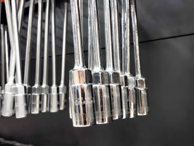 Bir set parlak krom kaplama altıgen soket anahtarı düzgün bir şekilde koyu gri arka planda asılı duruyor..