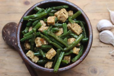 Kızarmış uzun fasulye ve tempeh, sarımsak ve kırmızı biberi ahşap arka planda beyaz tabakta karıştırın.