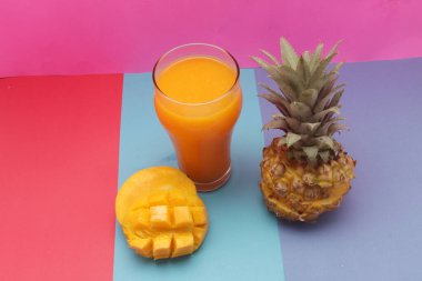 Pembe arka planda taze ananas ve mango suyu.