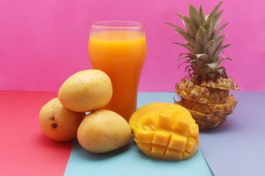 Pembe arka planda taze ananas ve mango suyu.