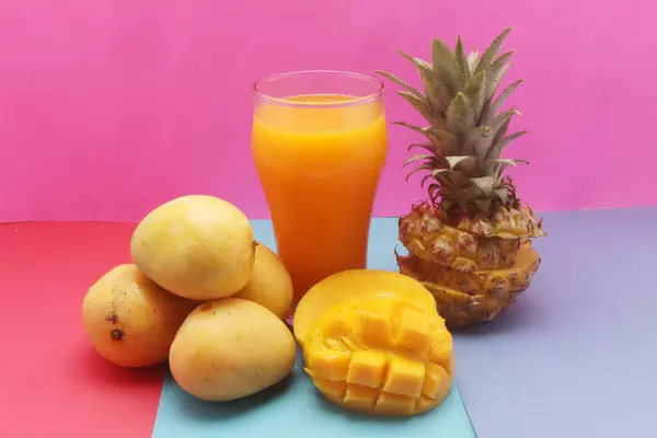 Pembe arka planda taze ananas ve mango suyu.