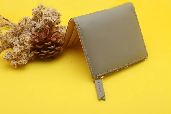 brown wallet with golden pen and a notebook on a yellow background with a branch