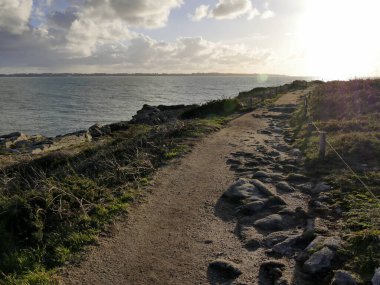 Deniz kenarındaki patika, yağmurlu, kışın güneşli bir gün, Britanya. Fransa 'da kıyı yolu, arkada Groix adası