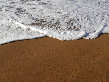 Beyaz deniz suyu köpüğü, altın kumsalda dalgalar.