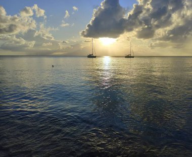 Sunset over guadeloupe seen from Anse Canot in Marie Galante, with swimmer in the sea and ships clipart