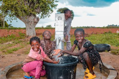 Abuja, Nijerya - 2 Ağustos 2021: Kırsal bir toplulukta güneşin altında temiz suyla oynarken mutluluk ve kahkaha ifade ederken eğlenen Afrikalı çocuklar. Neşeli ve Minnettar Çocuklar