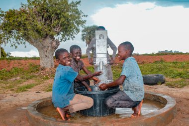 Abuja, Nijerya - 2 Ağustos 2021: Kırsal bir toplulukta güneşin altında temiz suyla oynarken mutluluk ve kahkaha ifade ederken eğlenen Afrikalı çocuklar. Neşeli ve Minnettar Çocuklar