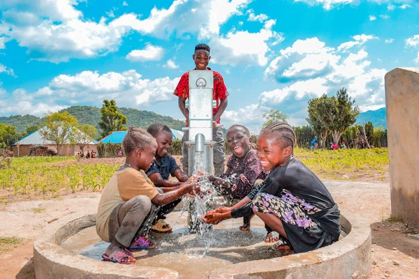 Abuja, Nijerya - 2 Ağustos 2021: Kırsal bir toplulukta güneşin altında temiz suyla oynarken mutluluk ve kahkaha ifade ederken eğlenen Afrikalı çocuklar. Neşeli ve Minnettar Çocuklar