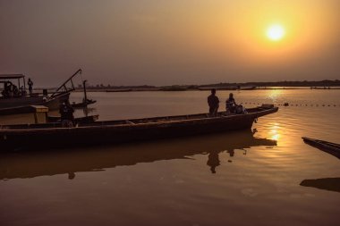 Delta State, Nijerya - 9 Aralık 2021 Nijer nehrinin kıyısında güzel bir Sunrise 'ı dengeleyen yerel kanolar yapıldı. Nehir kıyısında balıkçı tekneleri. Bir su yüzeyinde yansıma.