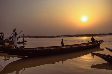 Delta State, Nijerya - 9 Aralık 2021 Nijer nehrinin kıyısında güzel bir Sunrise 'ı dengeleyen yerel kanolar yapıldı. Nehir kıyısında balıkçı tekneleri. Bir su yüzeyinde yansıma.