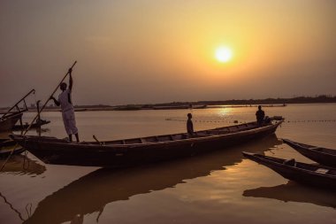 Delta State, Nijerya - 9 Aralık 2021 Nijer nehrinin kıyısında güzel bir Sunrise 'ı dengeleyen yerel kanolar yapıldı. Nehir kıyısında balıkçı tekneleri. Bir su yüzeyinde yansıma.