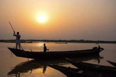 Delta State, Nijerya - 9 Aralık 2021 Nijer nehrinin kıyısında güzel bir Sunrise 'ı dengeleyen yerel kanolar yapıldı. Nehir kıyısında balıkçı tekneleri. Bir su yüzeyinde yansıma.