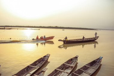 Delta State, Nijerya - 9 Aralık 2021 Nijer nehrinin kıyısında güzel bir Sunrise 'ı dengeleyen yerel kanolar yapıldı. Nehir kıyısında balıkçı tekneleri. Bir su yüzeyinde yansıma.