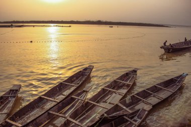 Delta State, Nijerya - 9 Aralık 2021 Nijer nehrinin kıyısında güzel bir Sunrise 'ı dengeleyen yerel kanolar yapıldı. Nehir kıyısında balıkçı tekneleri. Bir su yüzeyinde yansıma.