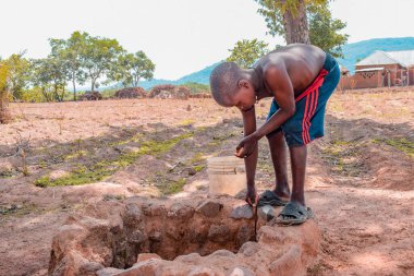 Jos East, Plateau State - 12 Mayıs 2021: Kırsal kesimdeki bir kuyudan su getiren Afrikalı çocuk. Çamurlu İşlenmemiş Su