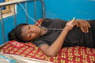 Opialu, Benue State - 6 Mart 2021: Siyahlar içindeki Afrikalı Gençler, tedavi görürken birincil sağlık merkezinde bir yatağın üzerinde yatıyor.