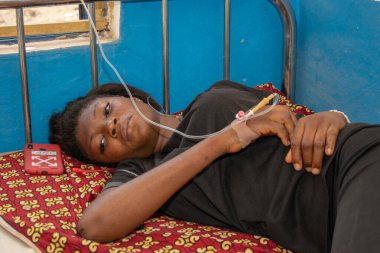 Opialu, Benue State - 6 Mart 2021: Siyahlar içindeki Afrikalı Gençler, tedavi görürken birincil sağlık merkezinde bir yatağın üzerinde yatıyor.