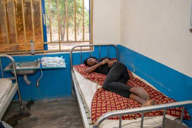 Opialu, Benue State - 6 Mart 2021: Siyahlar içindeki Afrikalı Gençler, tedavi görürken birincil sağlık merkezinde bir yatağın üzerinde yatıyor.