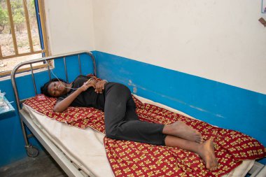 Opialu, Benue State - 6 Mart 2021: Siyahlar içindeki Afrikalı Gençler, tedavi görürken birincil sağlık merkezinde bir yatağın üzerinde yatıyor.