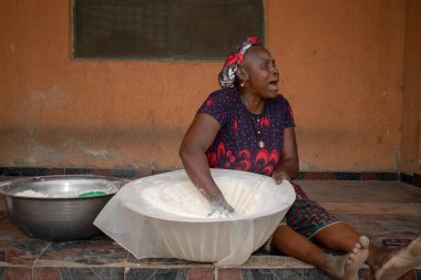 Opialu, Benue State, Nijerya - 6 Mart 2021: Gülümseyen Orta Çağ Afrikalı Kadın Cassava unu Süreci sırasında Yerde Çalışıyor ve Oturuyor (Garri)