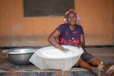 Opialu, Benue State, Nijerya - 6 Mart 2021: Gülümseyen Orta Çağ Afrikalı Kadın Cassava unu Süreci sırasında Yerde Çalışıyor ve Oturuyor (Garri)
