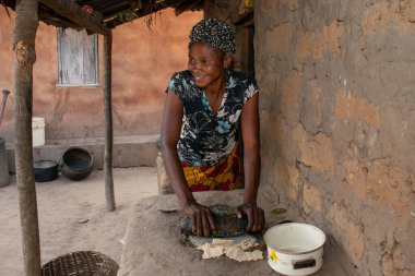 Opialu, Benue State - 6 Mart 2021: Afrikalı Kadın Çamur Evi 'nin yakınındaki Kavun ezmek için Yerel Öğütme Değirmeni' ni (Stone) kullanıyor.