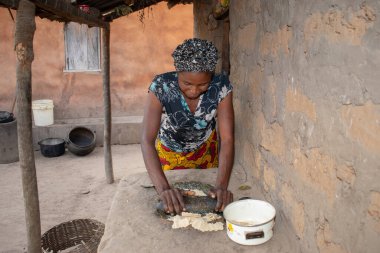 Opialu, Benue State - 6 Mart 2021: Afrikalı Kadın Çamur Evi 'nin yakınındaki Kavun ezmek için Yerel Öğütme Değirmeni' ni (Stone) kullanıyor.