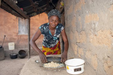 Opialu, Benue State - 6 Mart 2021: Afrikalı Kadın Çamur Evi 'nin yakınındaki Kavun ezmek için Yerel Öğütme Değirmeni' ni (Stone) kullanıyor.