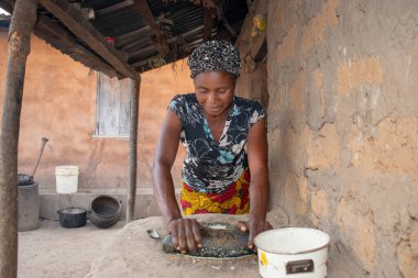 Opialu, Benue State - 6 Mart 2021: Afrikalı Kadın Çamur Evi 'nin yakınındaki Kavun ezmek için Yerel Öğütme Değirmeni' ni (Stone) kullanıyor.