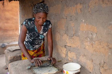 Opialu, Benue State - 6 Mart 2021: Afrikalı Kadın Çamur Evi 'nin yakınındaki Kavun ezmek için Yerel Öğütme Değirmeni' ni (Stone) kullanıyor.
