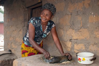 Opialu, Benue State - 6 Mart 2021: Afrikalı Kadın Çamur Evi 'nin yakınındaki Kavun ezmek için Yerel Öğütme Değirmeni' ni (Stone) kullanıyor.
