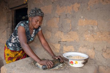 Opialu, Benue State - 6 Mart 2021: Afrikalı Kadın Çamur Evi 'nin yakınındaki Kavun ezmek için Yerel Öğütme Değirmeni' ni (Stone) kullanıyor.