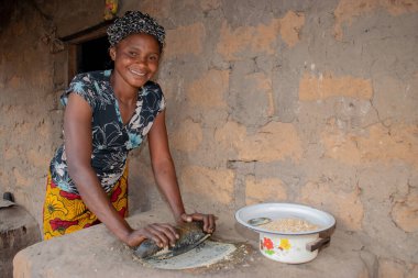 Opialu, Benue State - 6 Mart 2021: Afrikalı Kadın Çamur Evi 'nin yakınındaki Kavun ezmek için Yerel Öğütme Değirmeni' ni (Stone) kullanıyor.