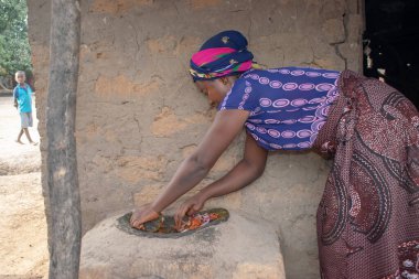 Opialu, Benue State - 6 Mart 2021: Afrikalı Kadın Çamur Evi 'nin yakınındaki Kavun ezmek için Yerel Öğütme Değirmeni' ni (Stone) kullanıyor.