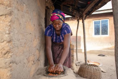 Opialu, Benue State - 6 Mart 2021: Afrikalı Kadın Çamur Evi 'nin yakınındaki Kavun ezmek için Yerel Öğütme Değirmeni' ni (Stone) kullanıyor.