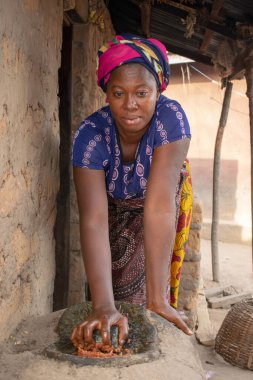 Opialu, Benue State - 6 Mart 2021: Afrikalı Kadın Çamur Evi 'nin yakınındaki Kavun ezmek için Yerel Öğütme Değirmeni' ni (Stone) kullanıyor.