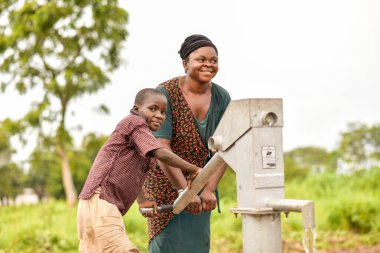 Talata, Plateau State - April 2, 2023: Indigenous African Woman and Boy Fetching Water from a Newly Built Indian Hand Pump. Community Members Fetching Water for Domestic Use. clipart
