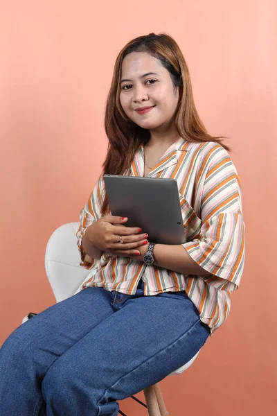 若い美しいアジアの女性 会社の労働者 笑顔と桃の背景と白い椅子に座ってデジタルタブレットを保持 — ストック写真