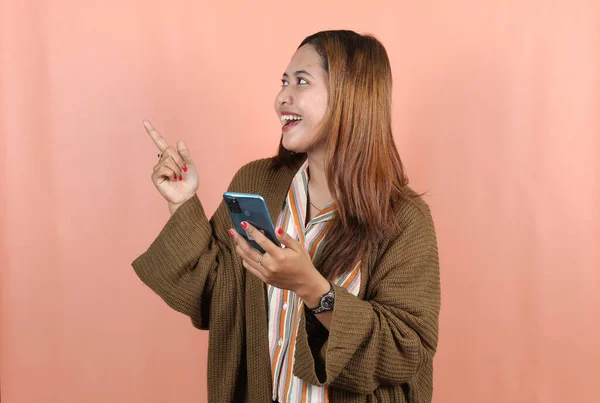 幸せな美しいアジアの女性は桃の背景に空の場所を指すとスマートフォンを保持 — ストック写真