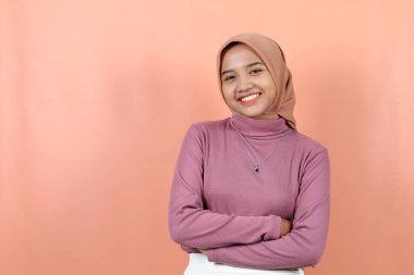 Mor kazaklı, gülümseyen güzel Asyalı kadın ellerini karnının üstünde tutuyor, önüne bakıyor, şeftali arka planda izole edilmiş bir his veriyor.