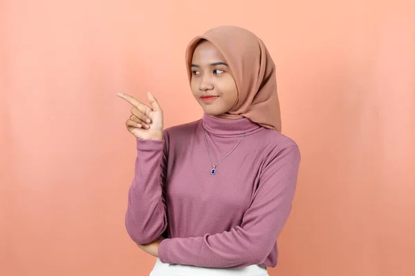 幸せな若いイスラム教徒のアジアの女性は 桃の背景に隔離された紫色のセーターで空の場所を指す — ストック写真