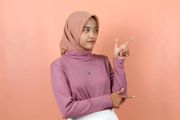 幸せな若いイスラム教徒のアジアの女性は 桃の背景に隔離された紫色のセーターで空の場所を指す — ストック写真