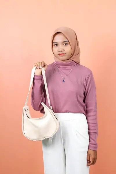 真剣な若い美しいアジアのムスリム女性が手元に白いファッションバッグを示しています — ストック写真