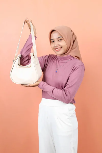 美しい若いアジアのイスラム教の女性は紫色のセーターを身に着けている白いファッションバッグを示すことを楽しみにしています — ストック写真