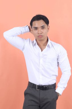 Genç Asyalı iş adamı beyaz bir gömlek giyiyor. Bir eliyle çizgilerden başını tutuyor diğer eliyle de pantolonunun cebine sokuyor.
