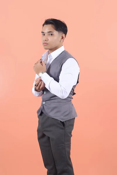 スーツのベストを着ているハンサムな若いアジアのビジネスマンは 桃の背景に自信を持って袖のボタンを調整する側面から見られます — ストック写真
