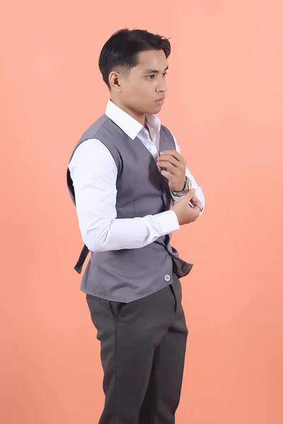 スーツのベストを着ているハンサムな若いアジアのビジネスマンは 桃の背景に自信を持って袖のボタンを調整する側面から見られます — ストック写真