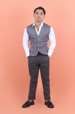 Yakışıklı ve gülümseyen Asyalı bir adam resmi bir yelek giyiyor kameraya bakıyor ve iki elini de cebine sokuyor.